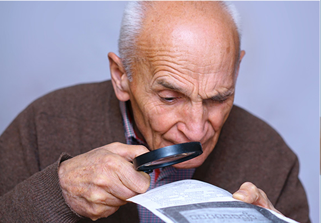 fotografía de un adulto mayor el cual tiene dificultades para ver utilizando como ayuda una lupa