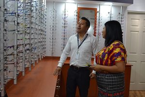 fotografía de la Óptica en centro de visión Chimaltenango, paciente tratando de elegir algún aro mientras un colaborador le indica cuales pueden ser las mejores opciones para ella.